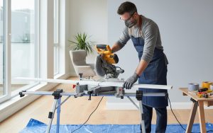 Bricoleur coupant une plinthe en angle avec une scie à onglet dans un intérieur moderne.